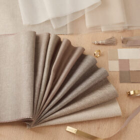 Neutral fabric swatches in beige and taupe arranged on a wooden surface, with a color card and measuring tape nearby.