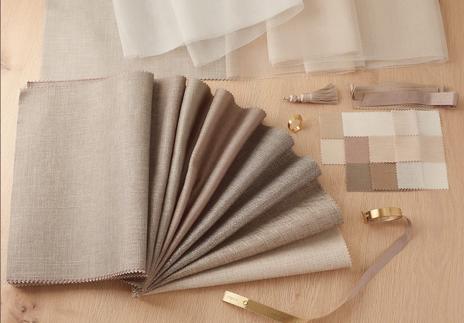 Neutral fabric swatches in beige and taupe arranged on a wooden surface, with a color card and measuring tape nearby.